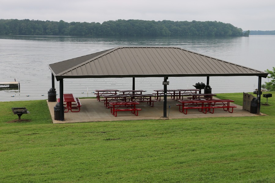 a picnic area with picnic tables and a covered area by a lake